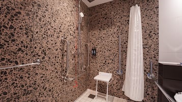 Ein modernes Badezimmer mit einer Wand mit Kieselstruktur, einer Dusche mit weißem Vorhang und einem kleinen, weißen Waschbecken.