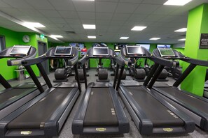 Une salle de sport équipée de plusieurs tapis de course, avec des murs verts et une horloge au mur.