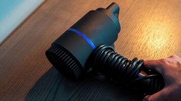 A cylindrical object with a blue stripe, a coiled cable, and a hand holding it.