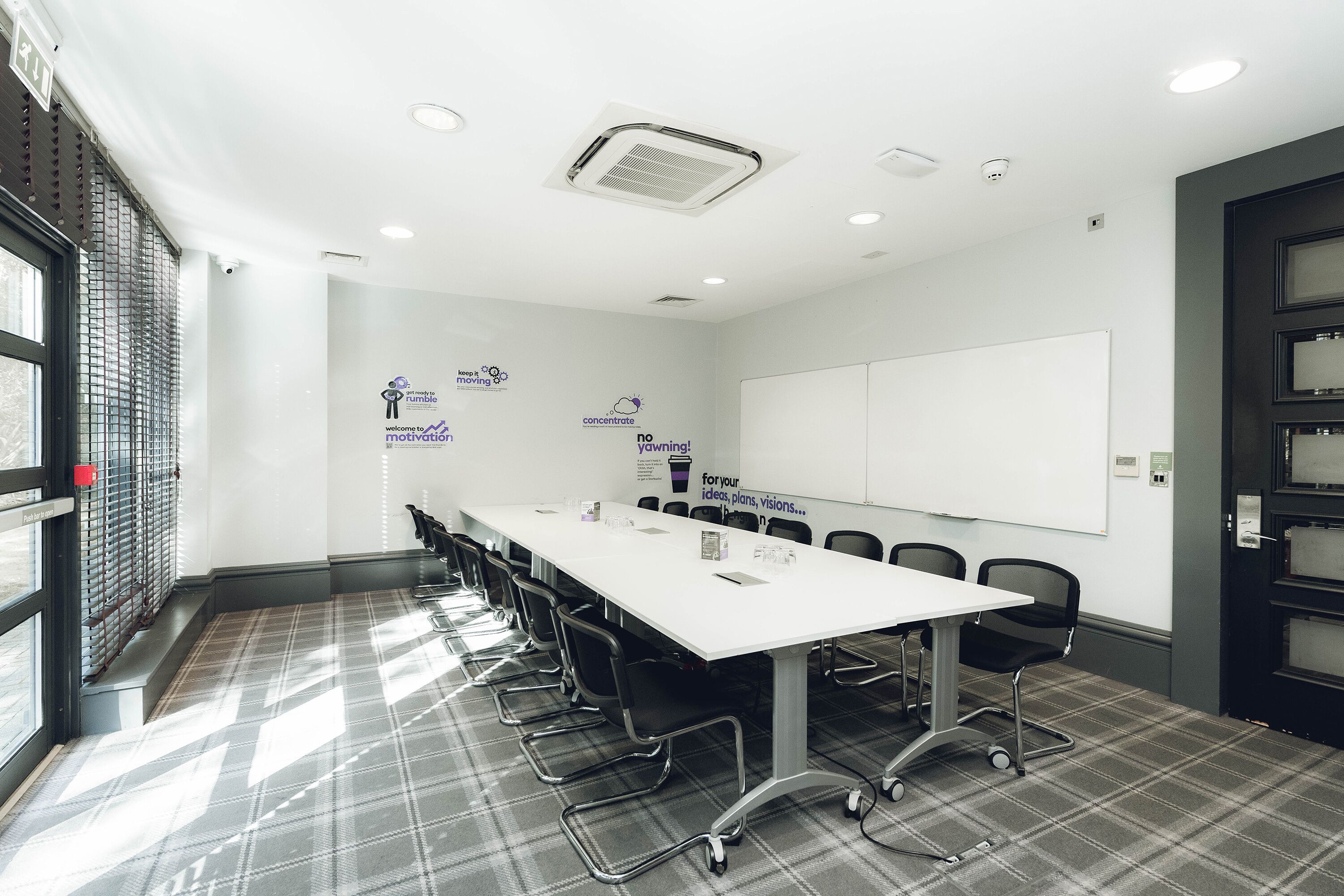 A conference room with a long table, chairs, a whiteboard, and motivational posters on the walls.