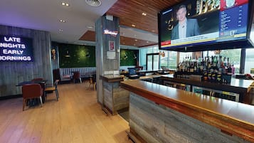 Una zona de bar con mostrador de madera, asientos y una pantalla grande mostrando un evento deportivo.