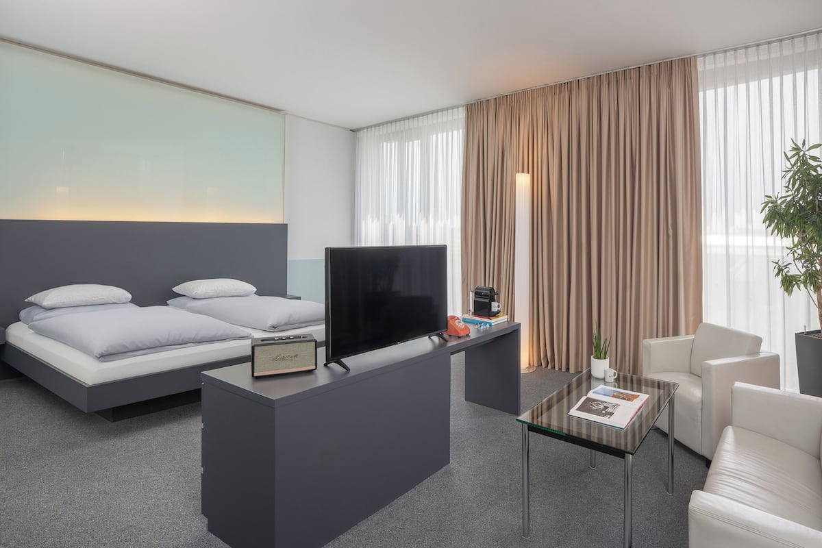 Une chambre d’hôtel moderne équipée d’un lit, d’un téléviseur à écran plat, d’une machine à café, d’une table en verre et d’une plante en pot.