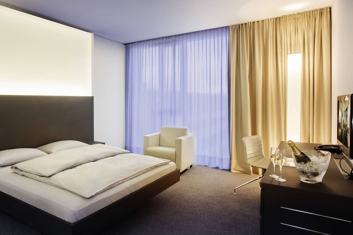 Une chambre d’hôtel comprenant un lit, deux chaises, un bureau avec une télévision et un minibar.