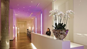 A reception area with a modern design, featuring a reception desk, a large decorative orchid planter, and a polished wooden floor. - INNSiDE by Meliá Düsseldorf Derendorf (Düsseldorf)