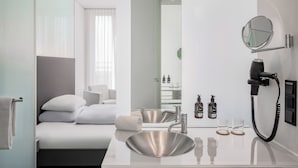 A modern hotel room with a large bed, a bathroom with a sink and mirror, and a hairdryer on the wall. - INNSiDE by Meliá Düsseldorf Derendorf (Düsseldorf)