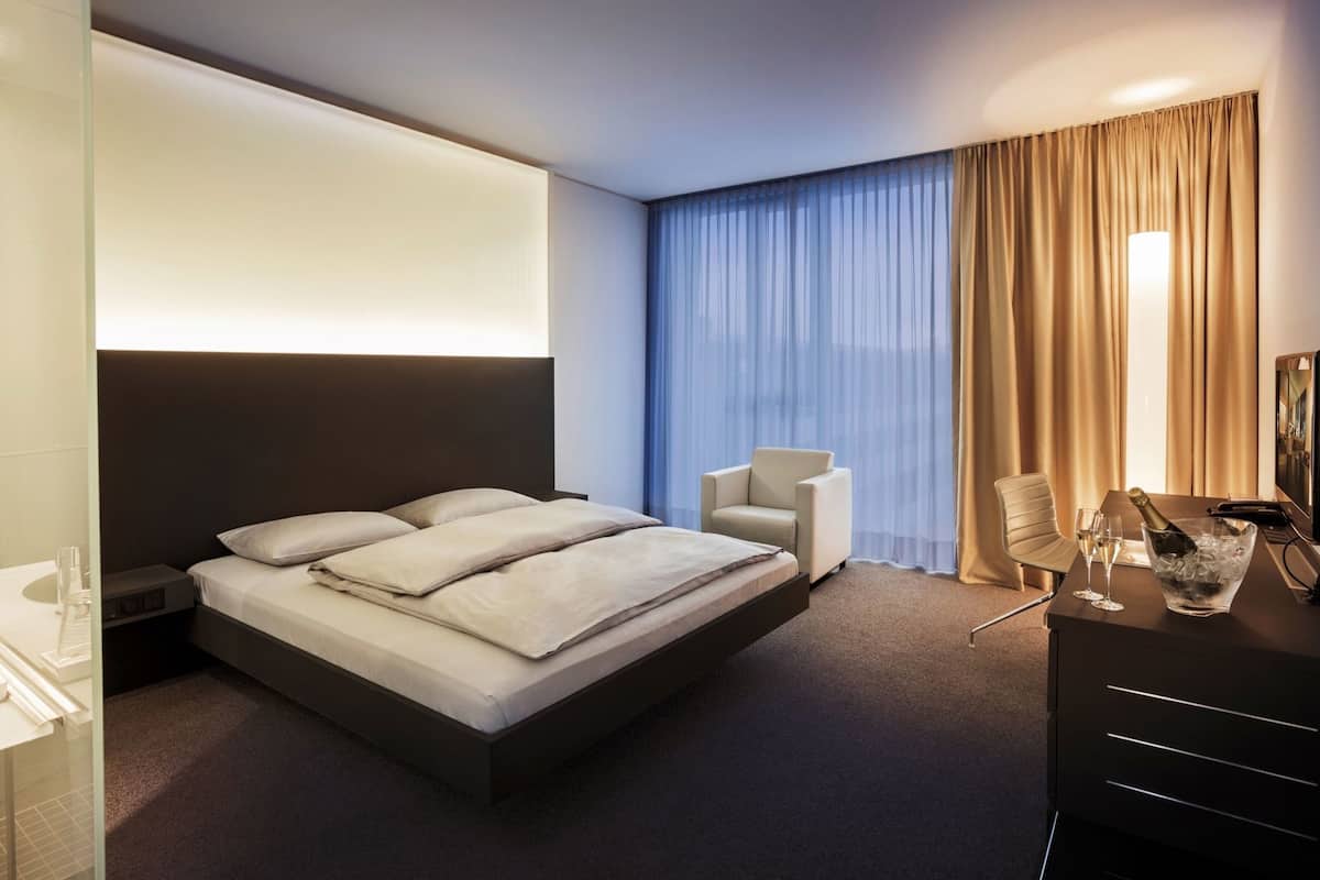 Une chambre d’hôtel moderne équipée d’un grand lit, d’un bureau avec une chaise, d’un minibar et d’une télévision.