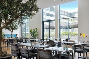 A modern restaurant with multiple dining tables, chairs, and large windows offering views of the cityscape. - INNSiDE by Meliá Düsseldorf Derendorf (Düsseldorf)