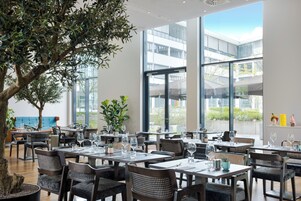 Un ristorante moderno con diversi tavoli, sedie e ampie finestre che offrono vista sulla città.