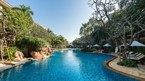A swimming pool with clear blue water, surrounded by lush greenery and palm trees.