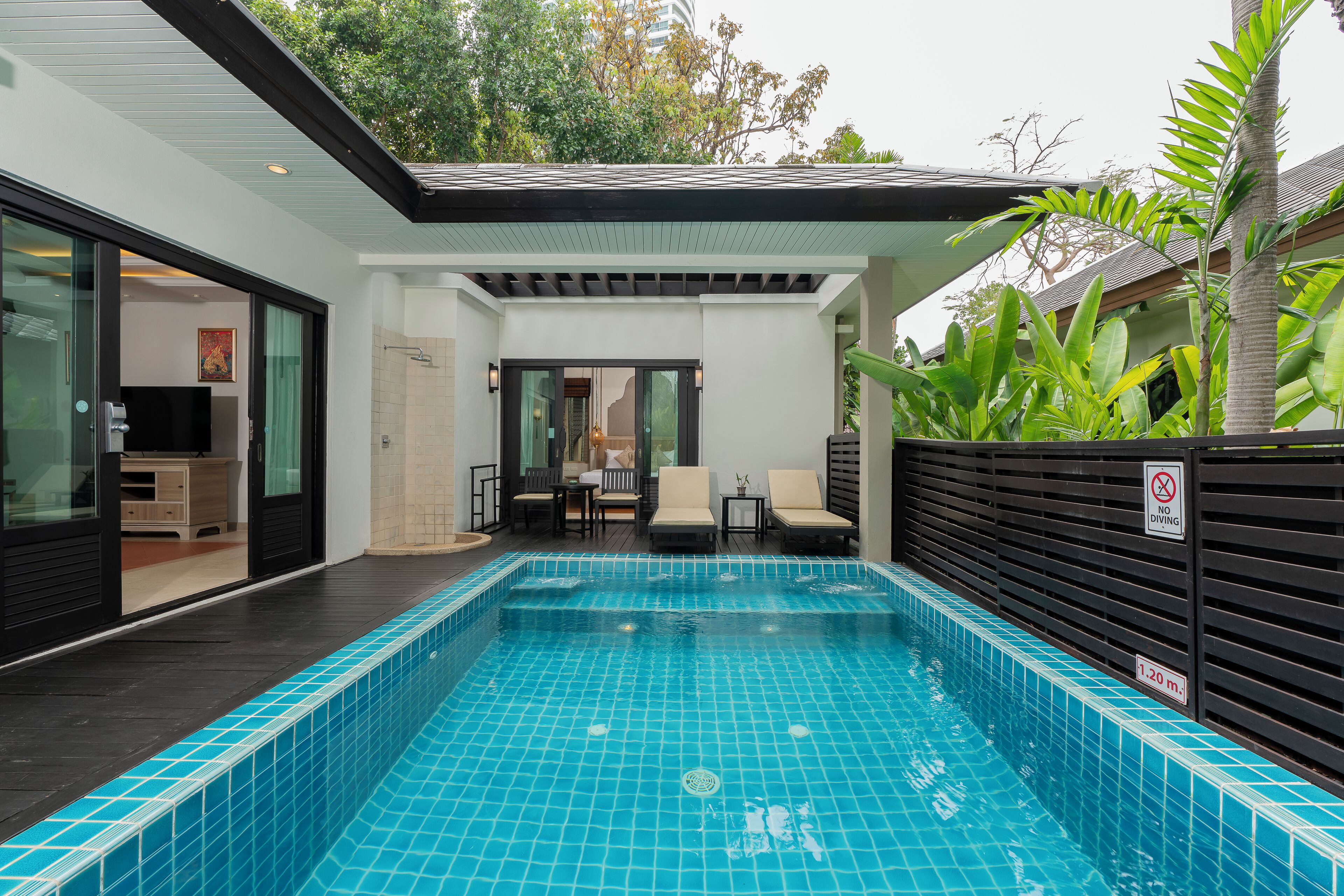 Piscina interior moderna com chão em azulejo, placa de proibição de mergulho e área de estar com cadeiras e mesa.