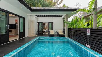 Piscina interior moderna com chão em azulejo, placa de proibição de mergulho e área de estar com cadeiras e mesa.
