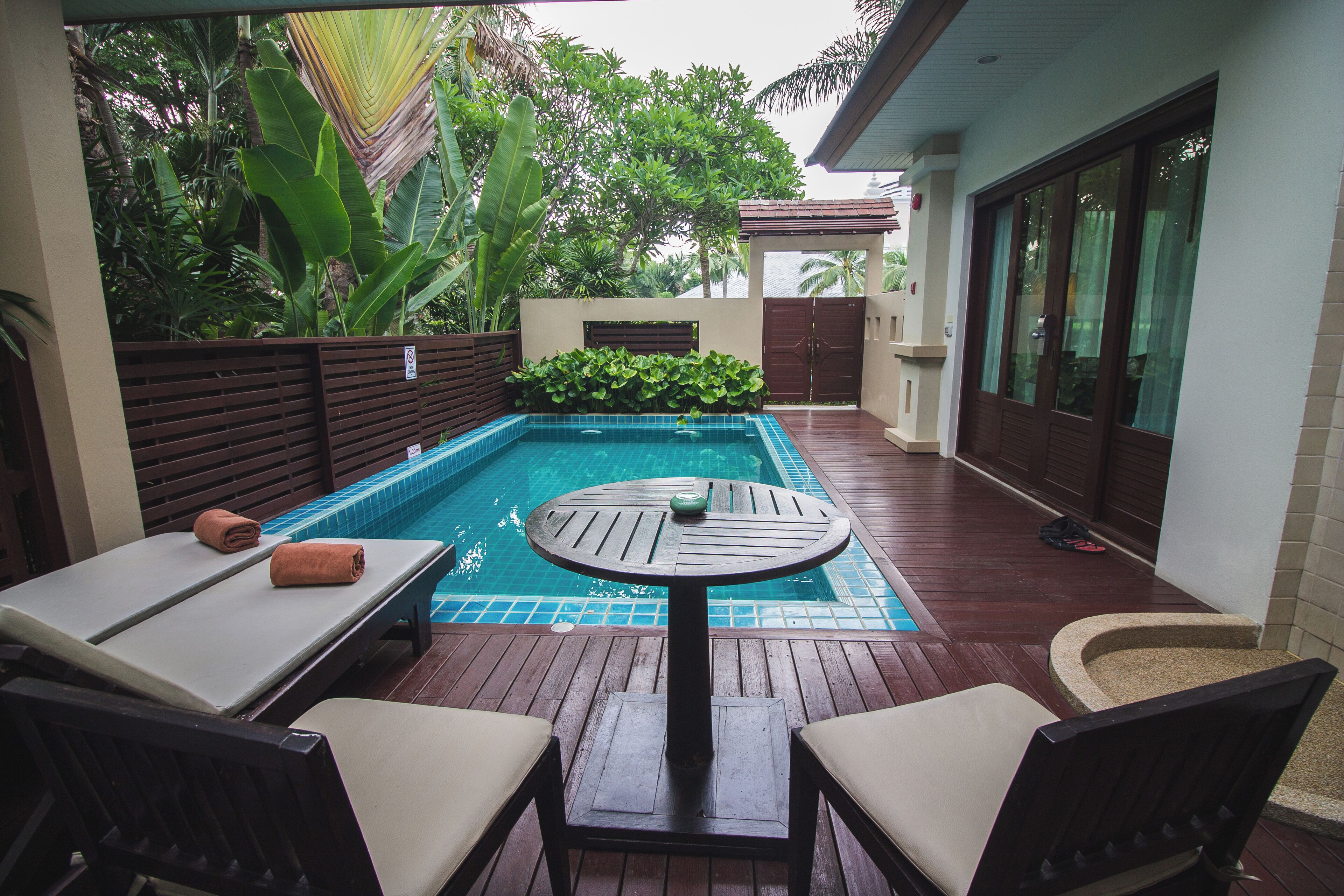 A poolside area with a wooden deck, a small round table, and two lounge chairs.