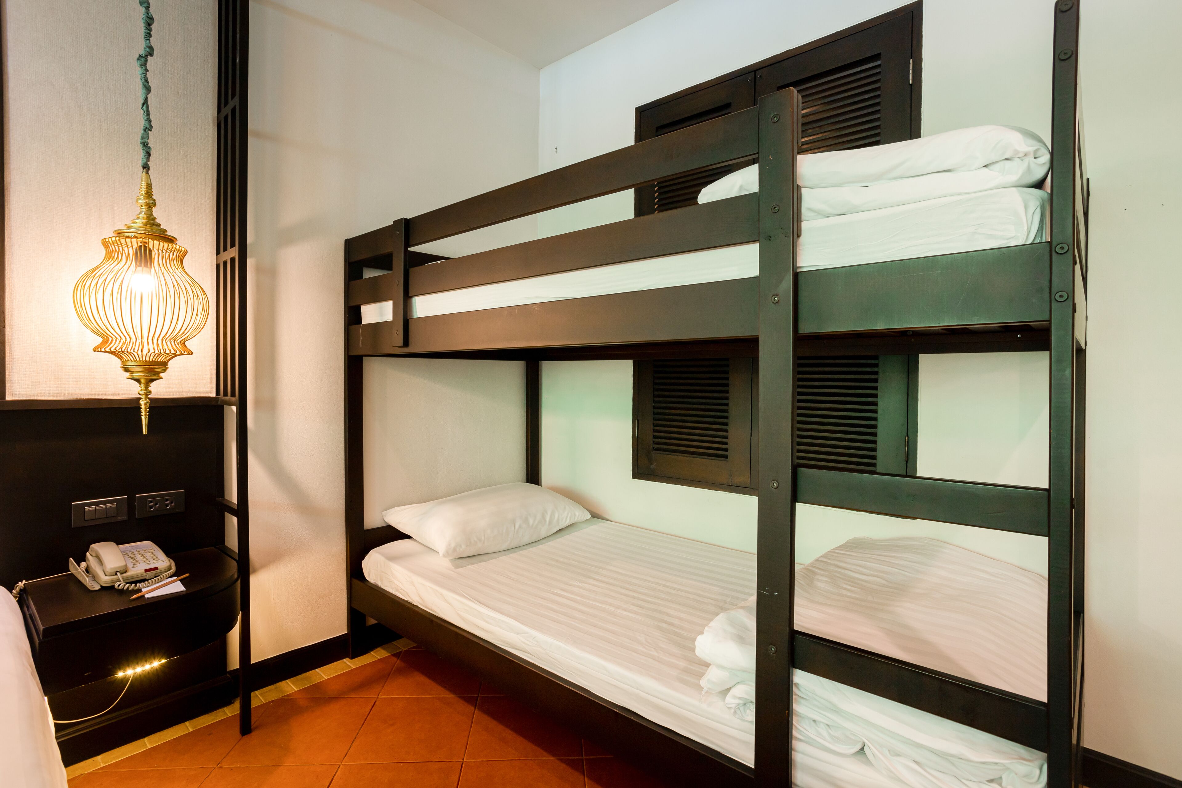 Une chambre avec un lit superposé, un luminaire suspendu, une table de chevet avec un téléphone et une étagère fixée au mur.