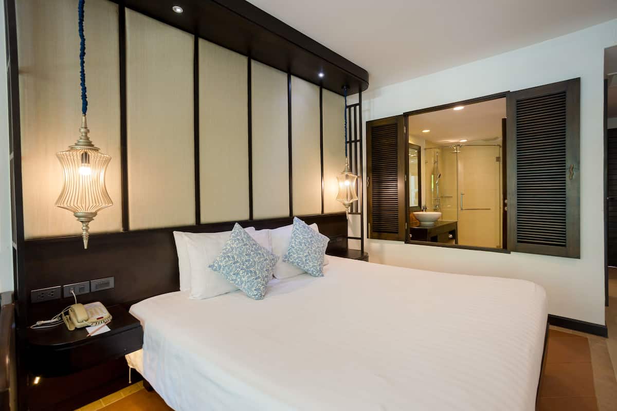 Quarto de hotel com cama grande, mesa de cabeceira com telefone e espelho refletindo o banheiro.