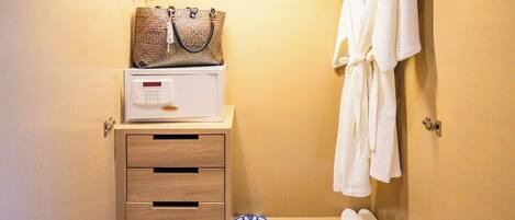 A hotel bathroom with a wooden vanity, a microwave, a robe, slippers, and a towel rack.