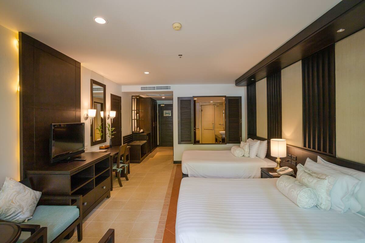 Quarto de hotel com televisão, duas camas, escrivaninha e banheiro.