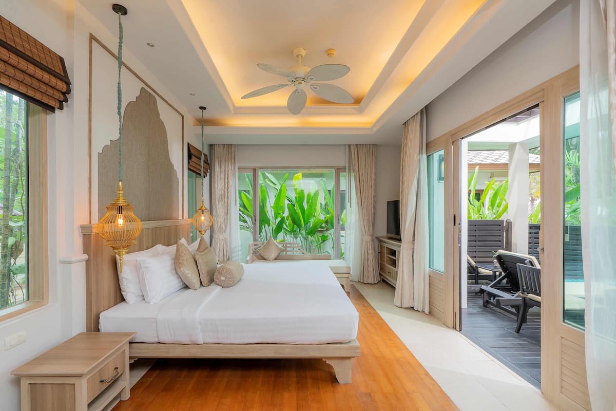 Quarto com cama grande, mesas de cabeceira, ventilador de teto e vista para o exterior.