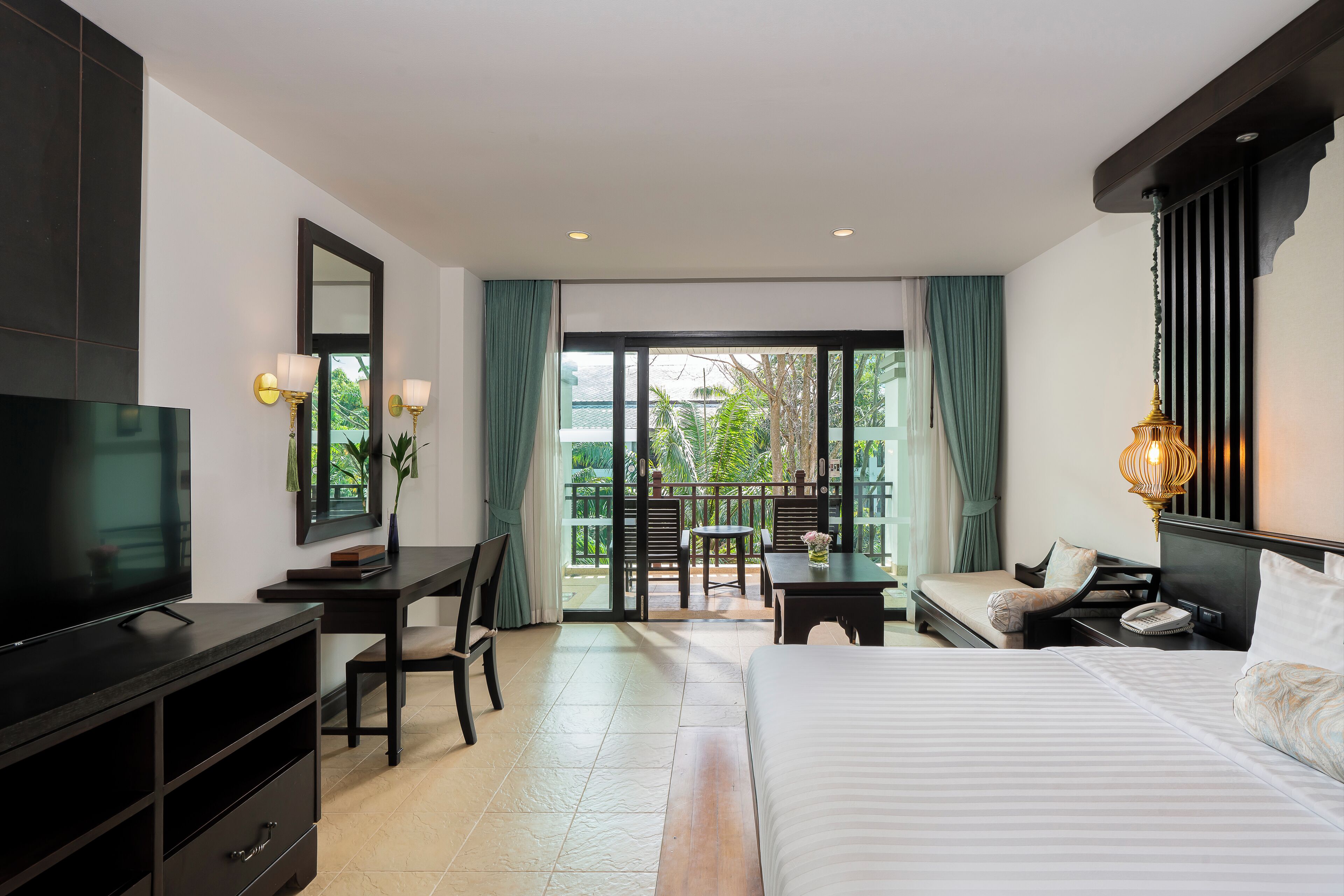 A hotel room with a bed, a desk, a TV, and a balcony with a view of greenery.