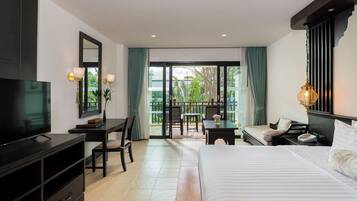 A hotel room with a bed, a desk, a TV, and a balcony with a view of greenery.