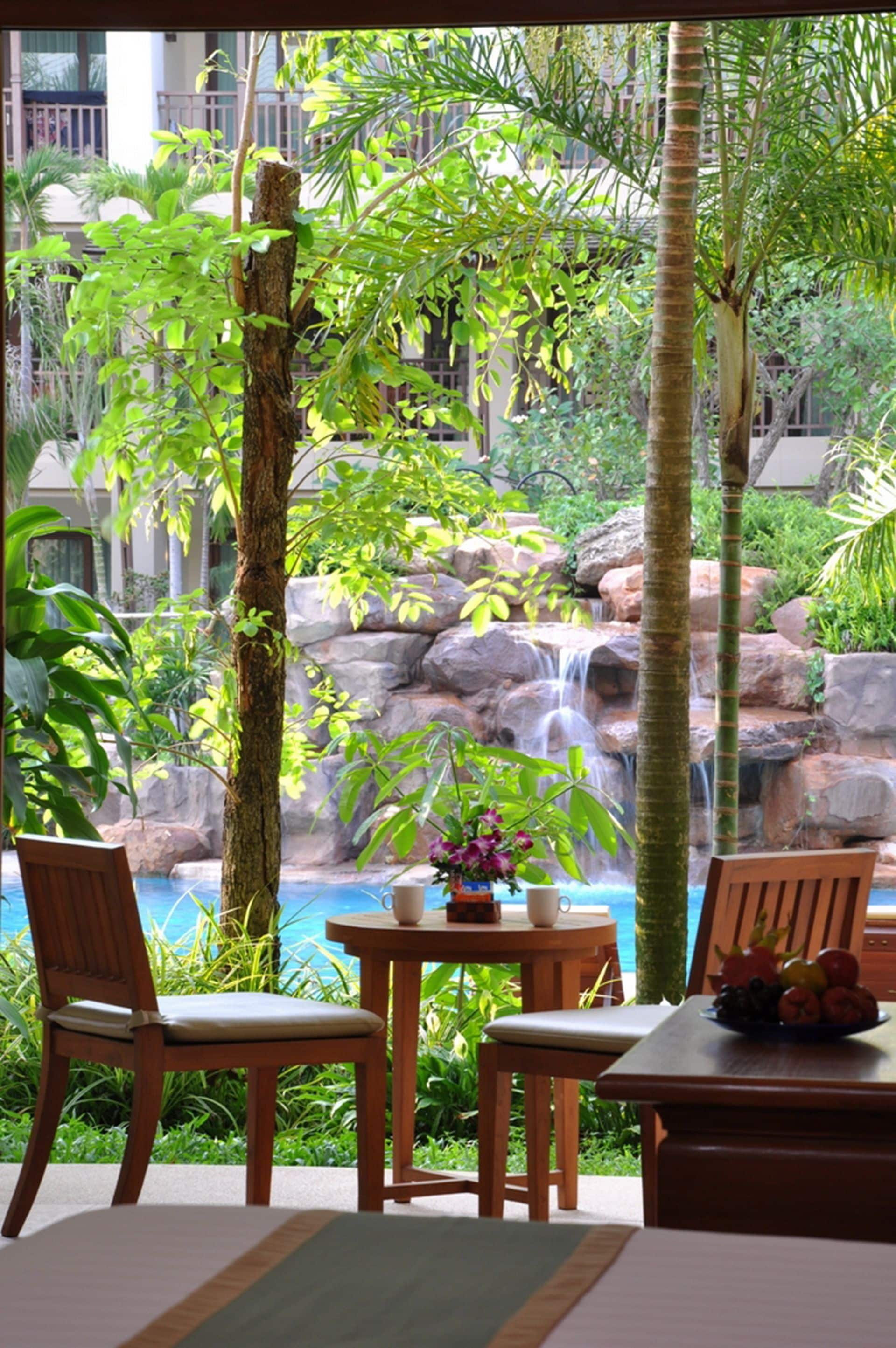 A tropical indoor garden with a waterfall, seating area, and a view of the ocean.