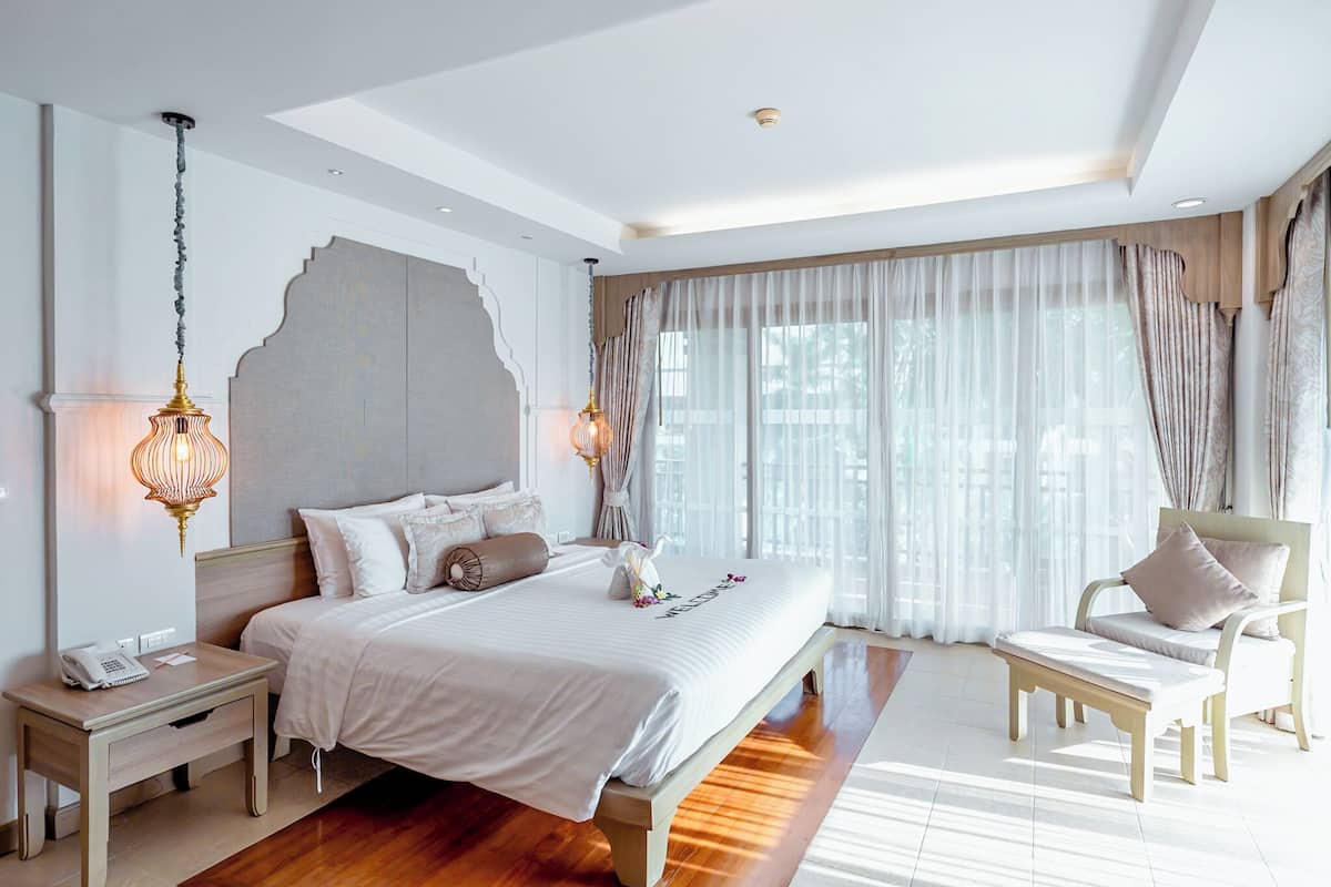 Quarto moderno com uma cama grande, mesas de cabeceira, uma cadeira e uma janela ampla com cortinas.