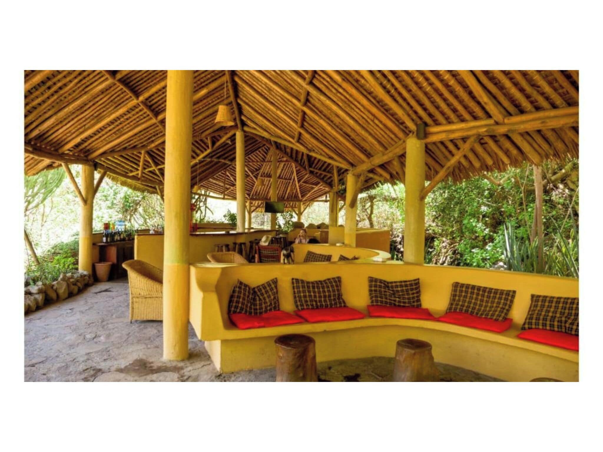 A covered outdoor seating area with a thatched roof, yellow walls, and red cushions.