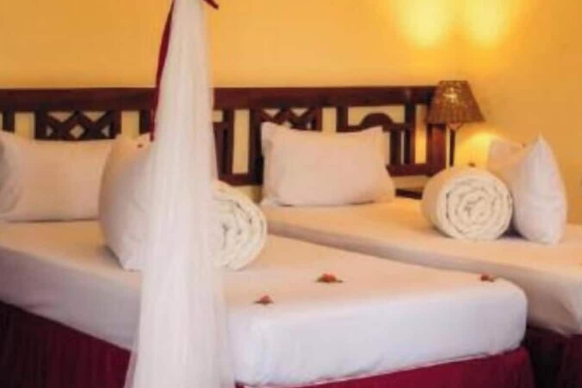 Habitación de hotel con cama a dosel, dos almohadas, una toalla enrollada y una lámpara en la mesita de noche.