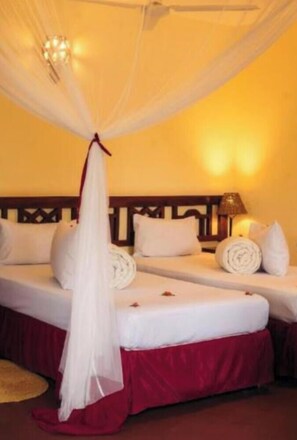 A hotel room with a canopy bed, two pillows, a rolled towel, and a lamp on the nightstand.
