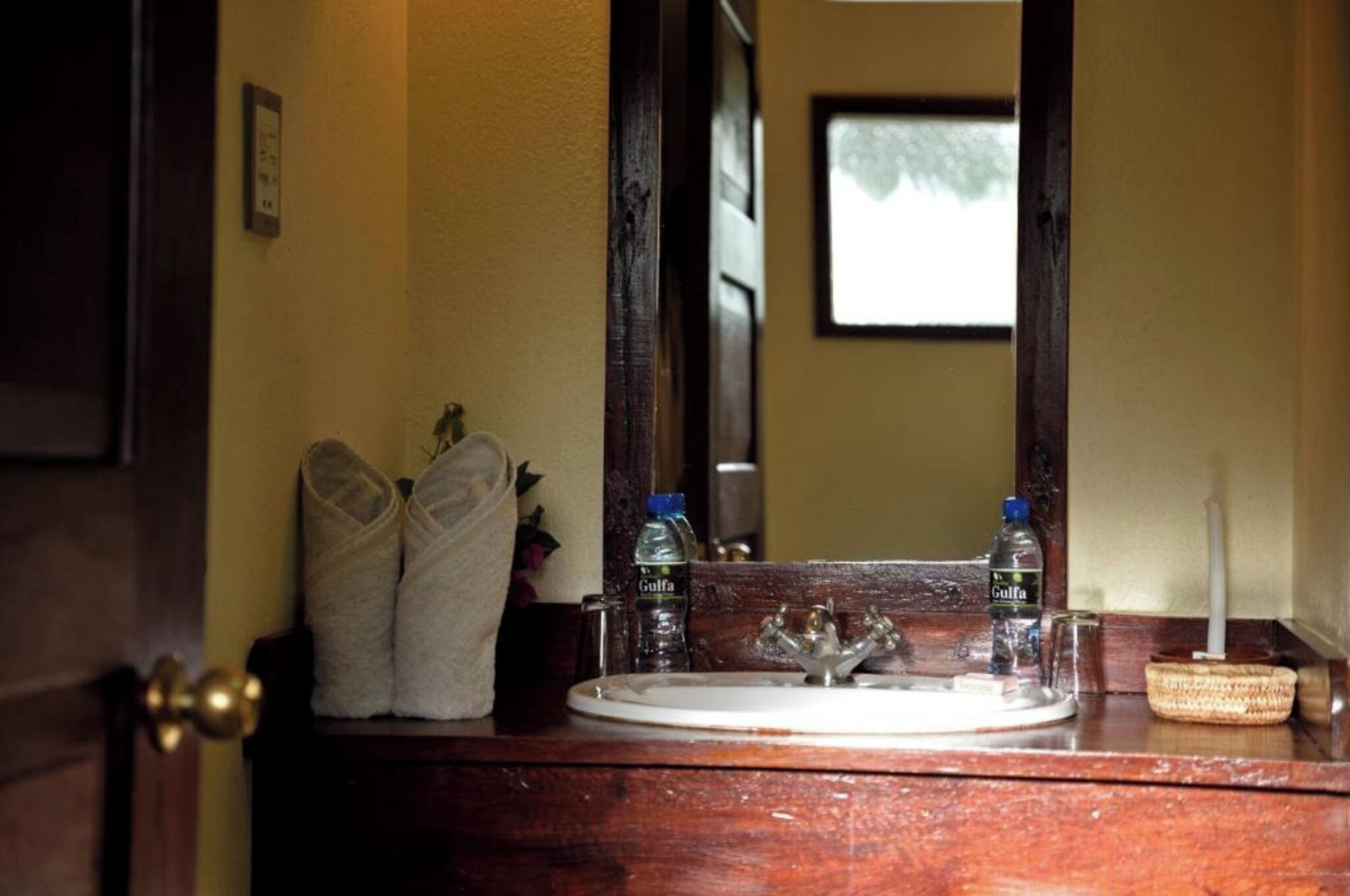 A bathroom vanity with a mirror, two bottles of water, a towel, and a candle.