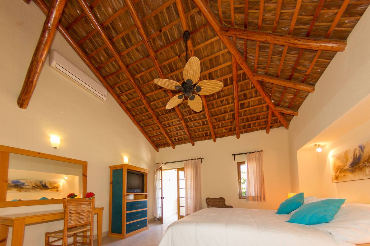 A bedroom with a sloped ceiling, a bed with blue pillows, a television, and a desk with a chair.