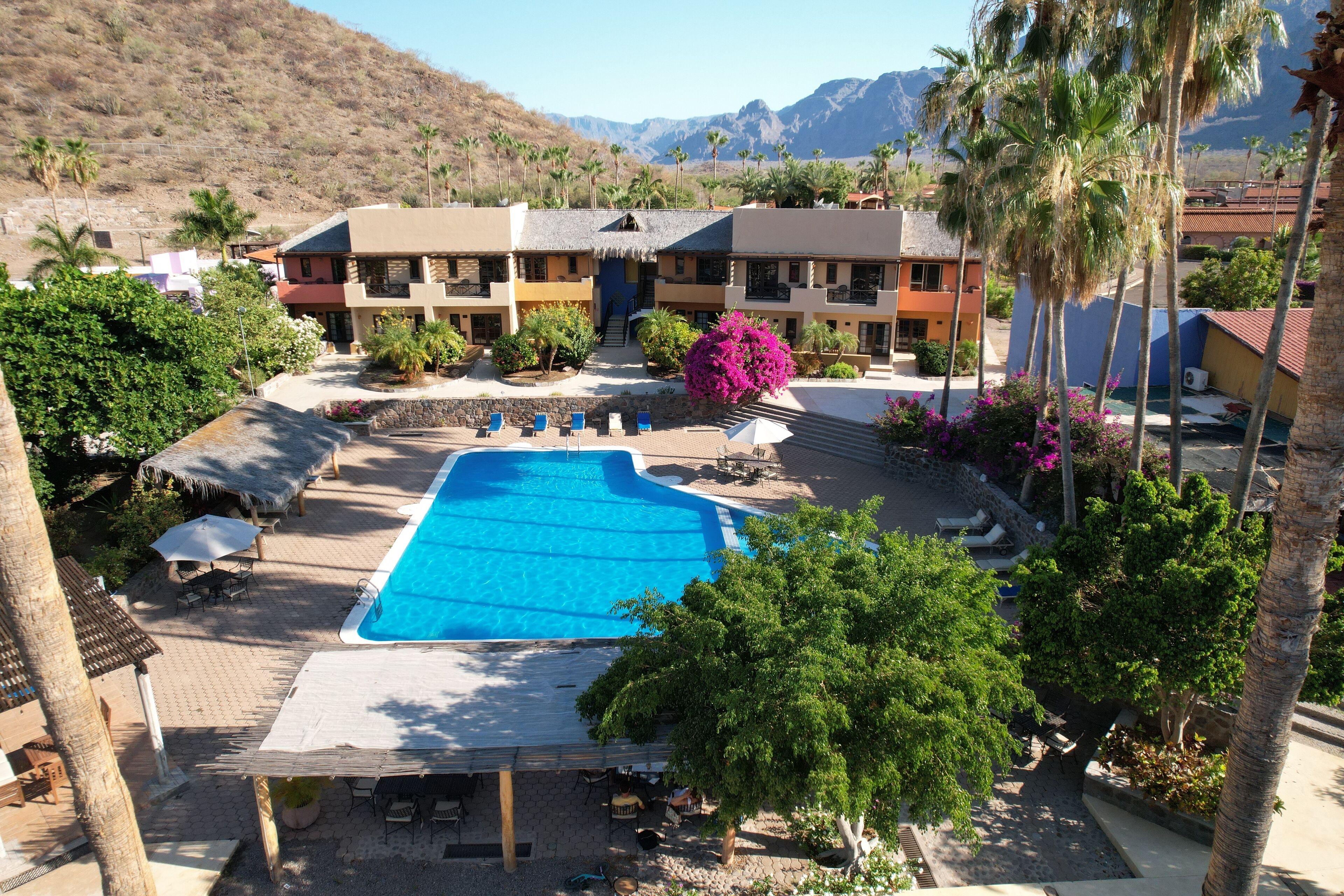 A resort with a swimming pool, outdoor seating, and a mountain backdrop.