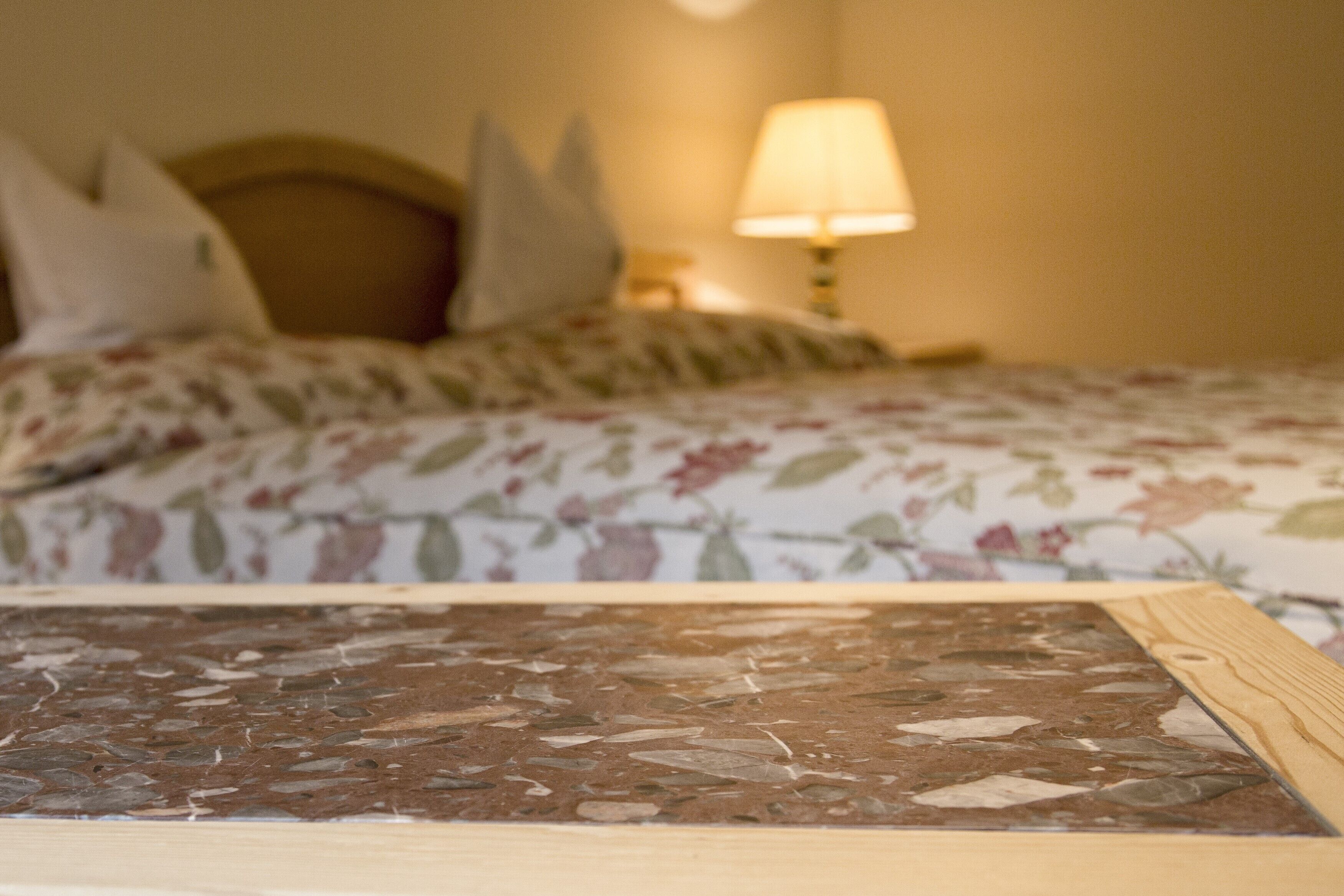 Una cama con ropa de cama floral, un cabecero de madera y una mesita de noche con una lámpara.