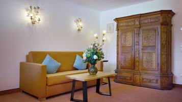 Una habitación con sofá, una mesa con un jarrón, apliques de pared y un armario de madera.