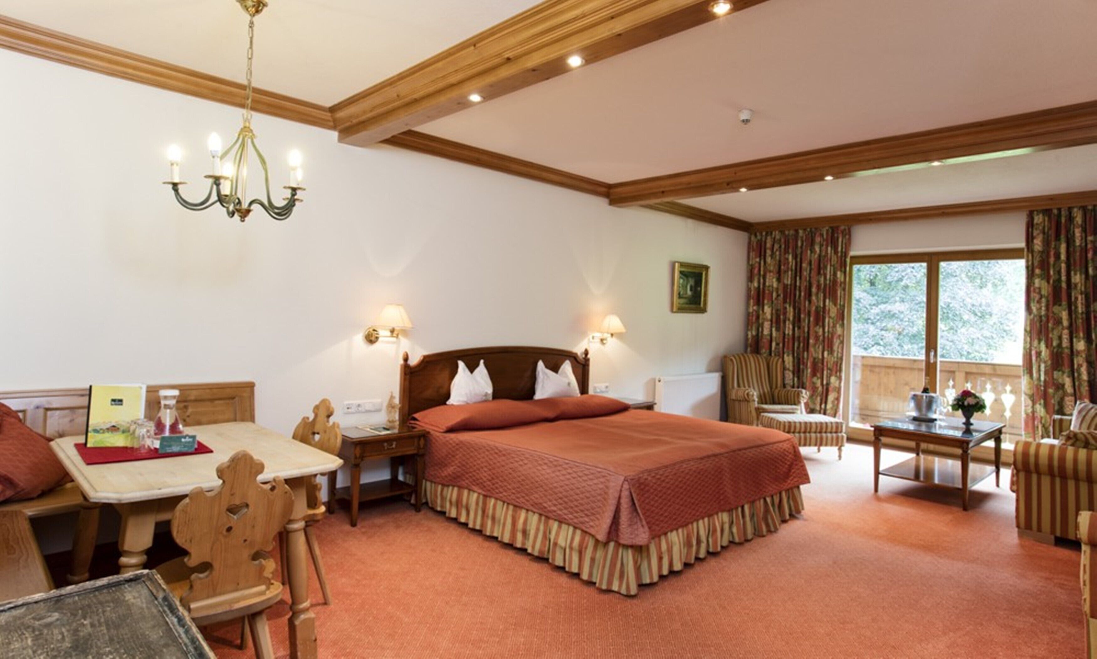 A hotel room with a large bed, a desk with a chair, a dining table, and a window with curtains.