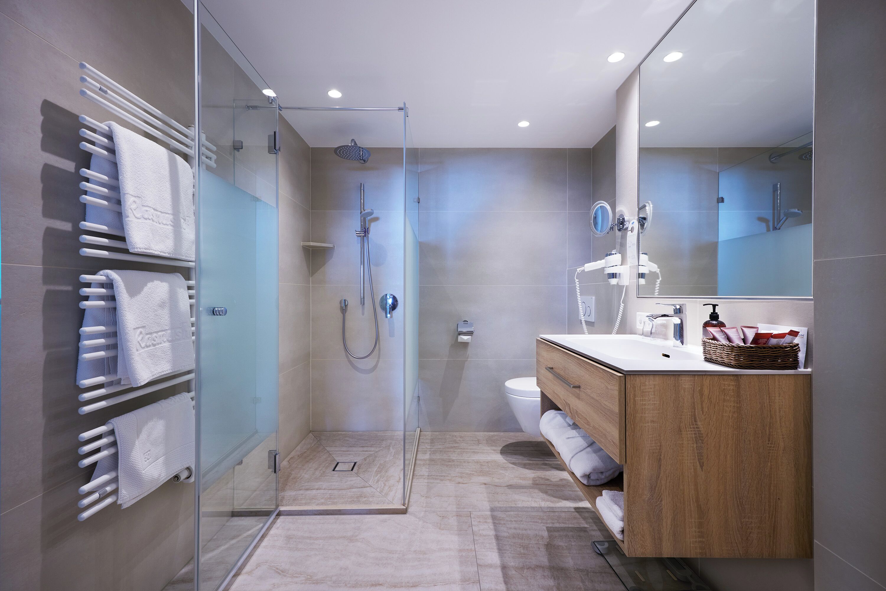 Une salle de bain moderne dotée d’une douche à parois de verre, d’un meuble-lavabo en bois et d’un porte-serviettes avec plusieurs serviettes.