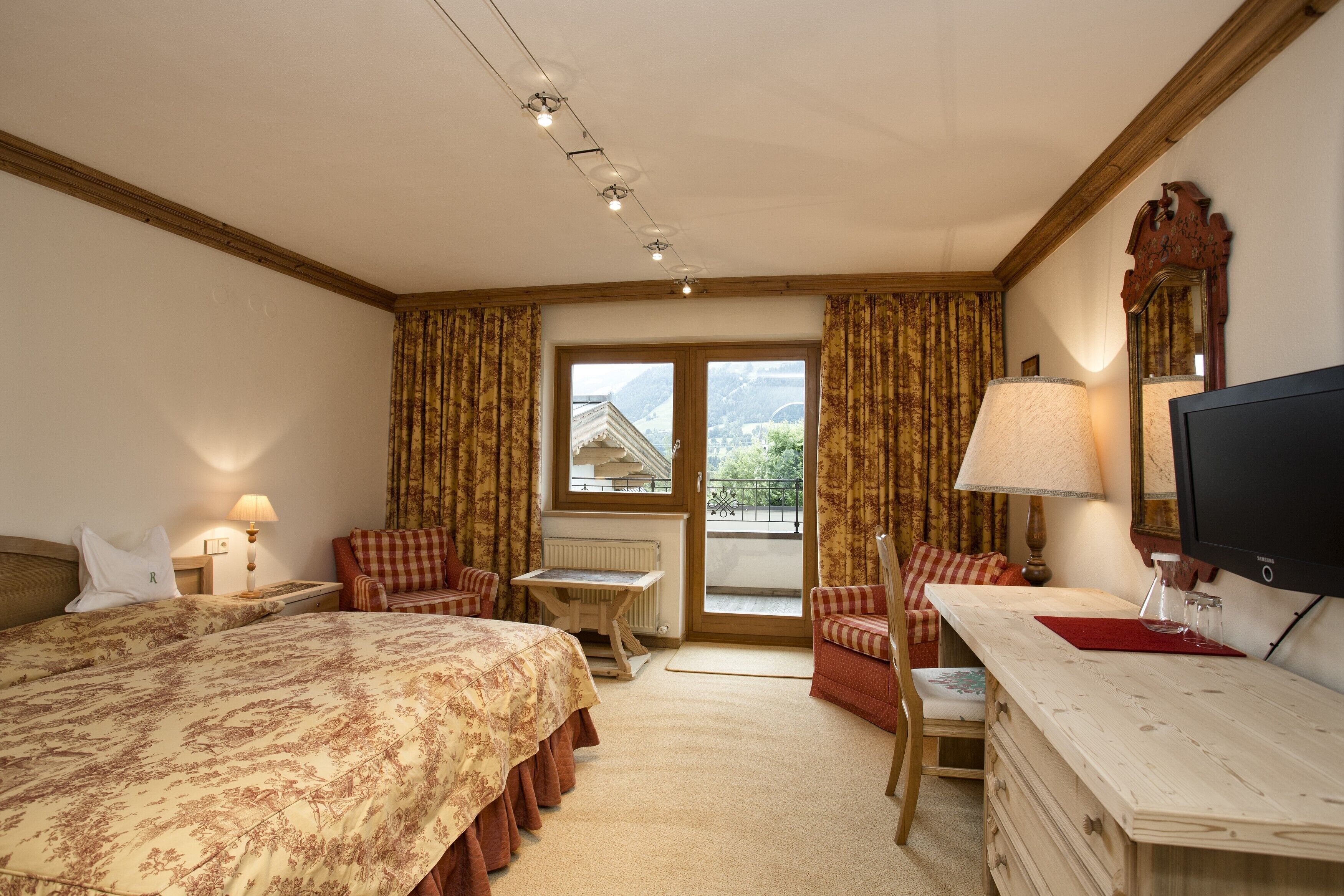 A hotel room with a large bed, a desk, a chair, a TV, and a window with curtains.