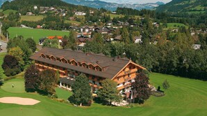 Un gran edificio de madera con múltiples balcones, rodeado de exuberante vegetación y un campo de golf.