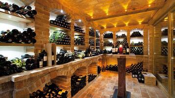 Una bodega con múltiples estantes y botelleros llenos de vino, paredes de piedra y una columna de madera central.