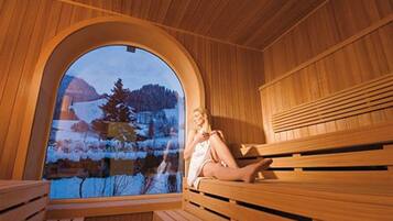 Una sauna con bancos de madera y un amplio ventanal de arco que ofrece vistas a un paisaje nevado.
