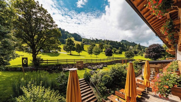 Una terraza de madera con mobiliario exterior, vista a un campo de golf y un paisaje montañoso.