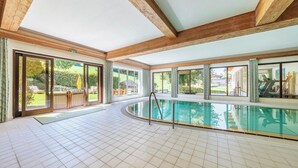 Una amplia piscina interior con suelo de baldosas, vigas de madera y ventanas grandes que ofrecen vistas al exterior.