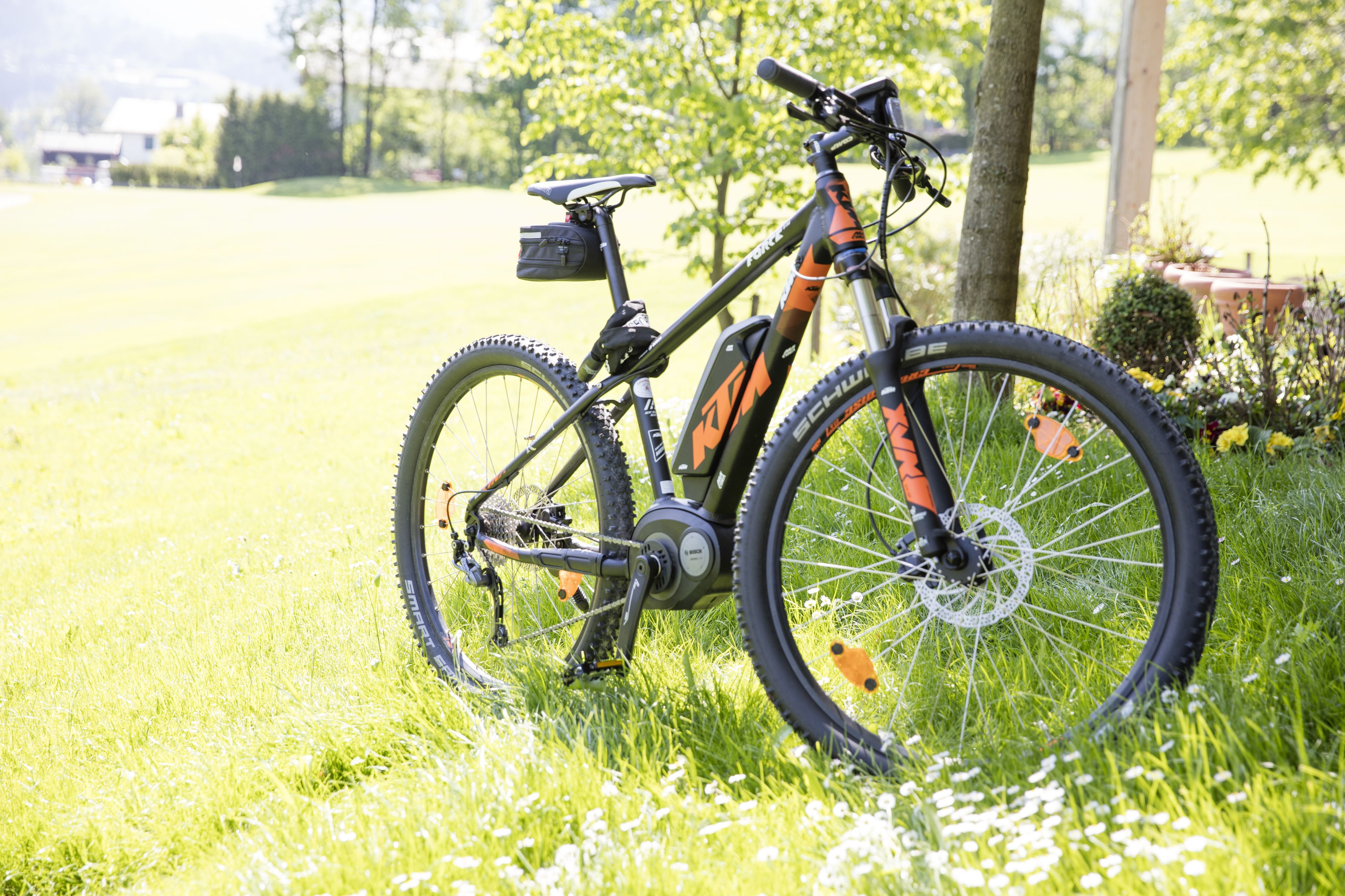 A mountain bike parked on grass with a tree and a house in the background.