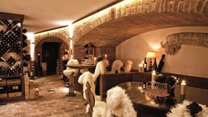 Un interior acogedor y rústico con paredes de ladrillo, un botellero de madera, cómodas sillas blancas y una mesa iluminada con velas.