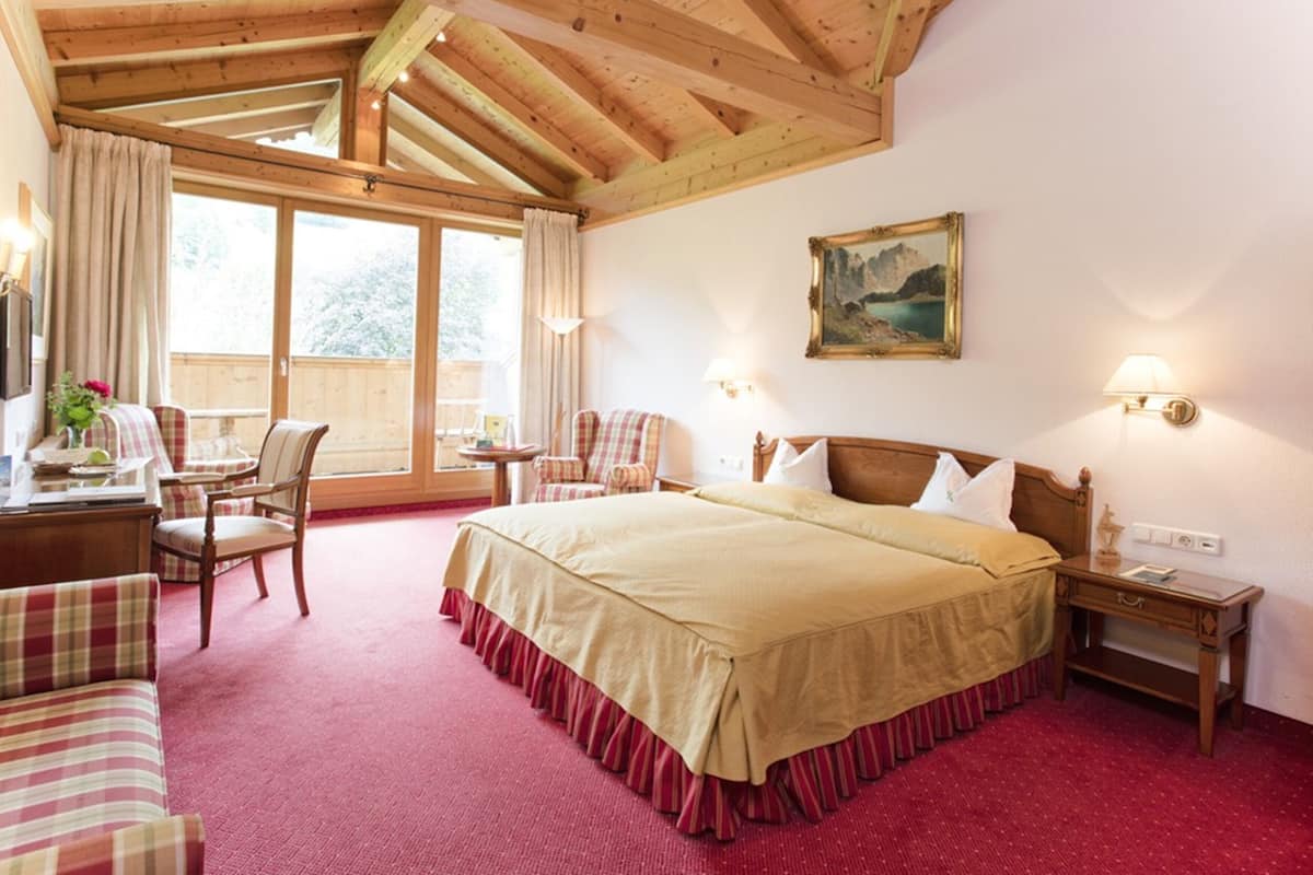 Une chambre d’hôtel avec un grand lit, des poutres en bois au plafond, un tableau accroché au mur et une vue sur l’extérieur par la fenêtre.