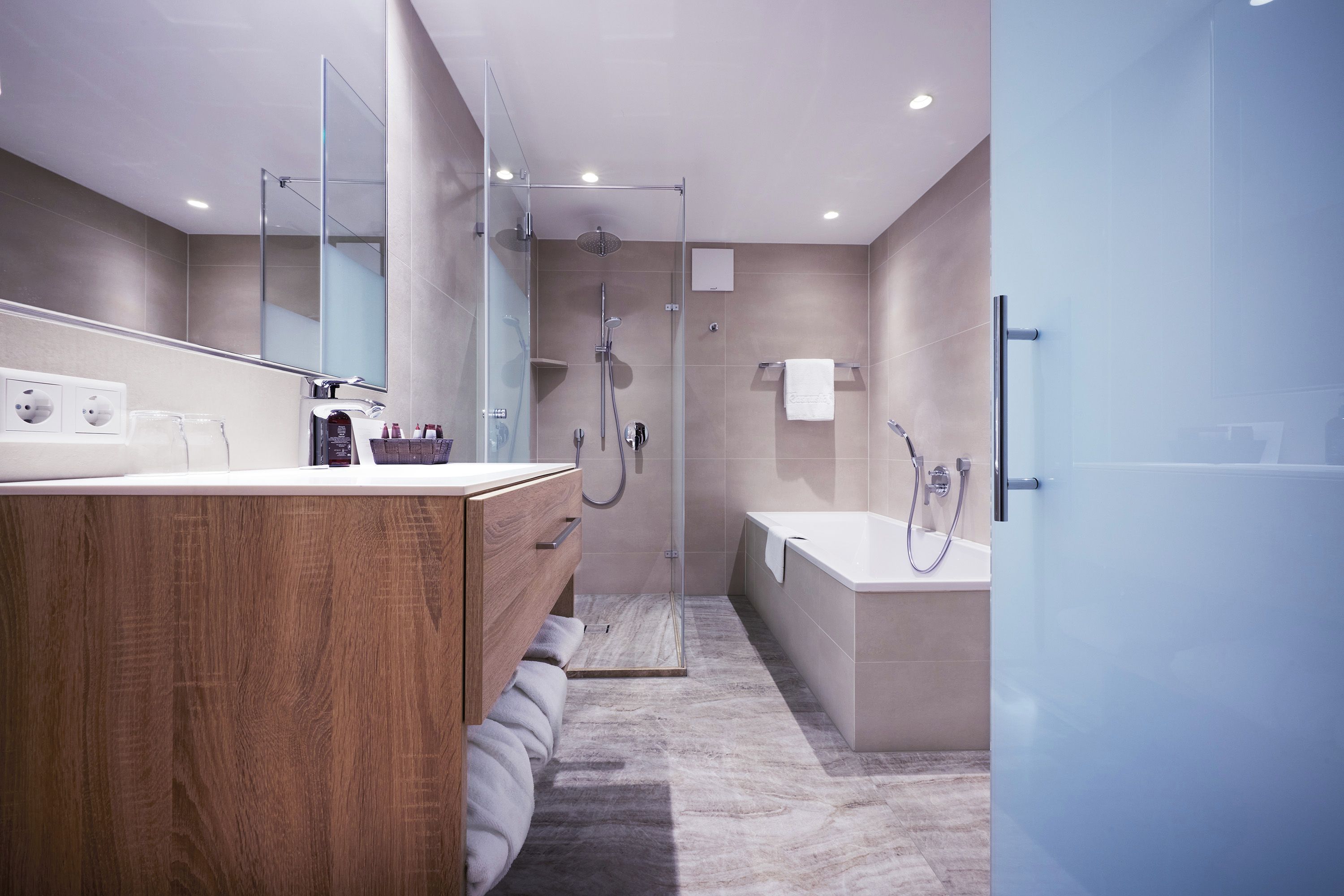 A modern bathroom with a wooden vanity, a glass shower enclosure, and a separate bathtub.