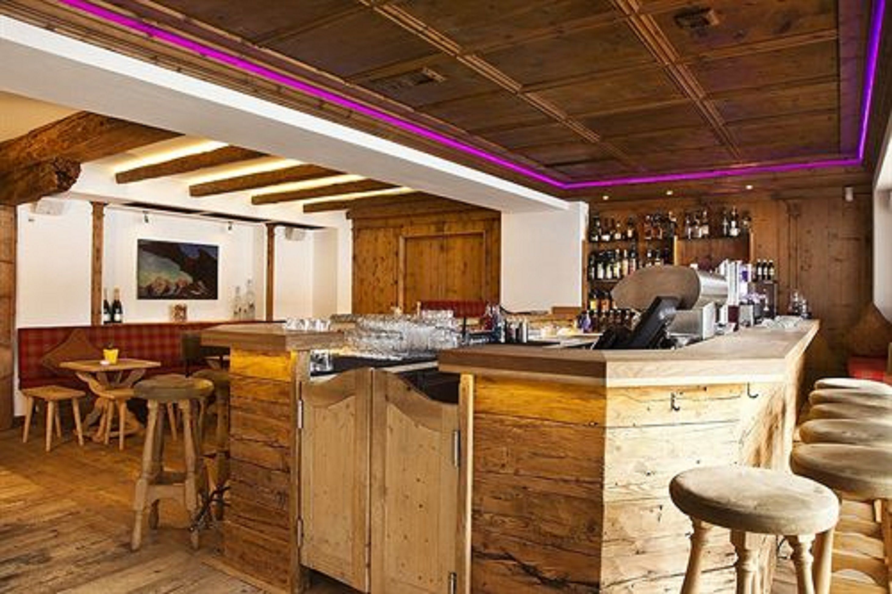 A rustic bar area with wooden beams, a bar counter, stools, and a wall of liquor bottles.