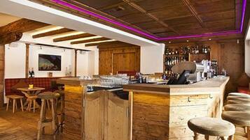 A rustic bar area with wooden beams, a bar counter, stools, and a wall of liquor bottles.