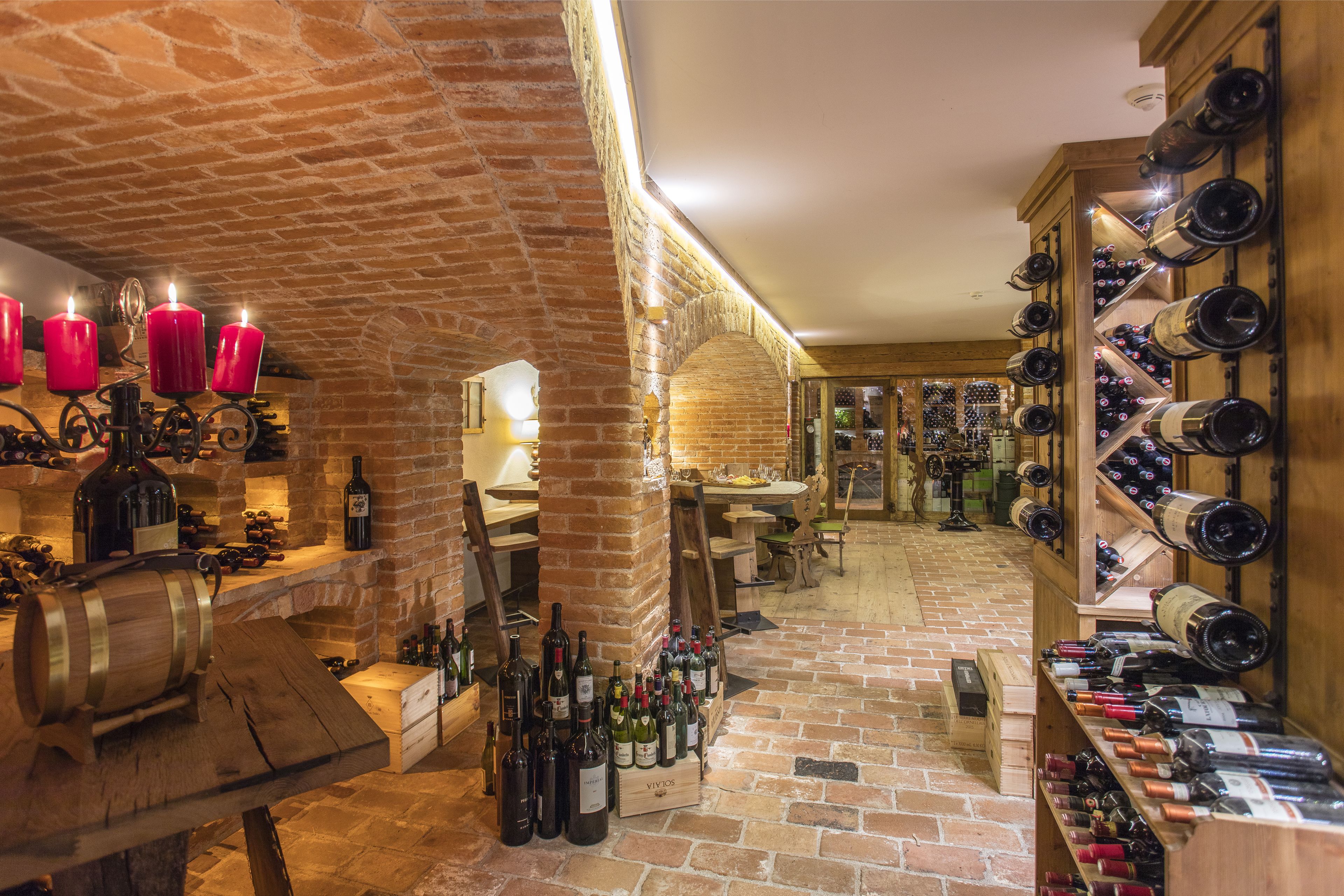 A wine cellar with wooden racks and shelves filled with wine bottles, a brick wall, and a wooden table with wine barrels.