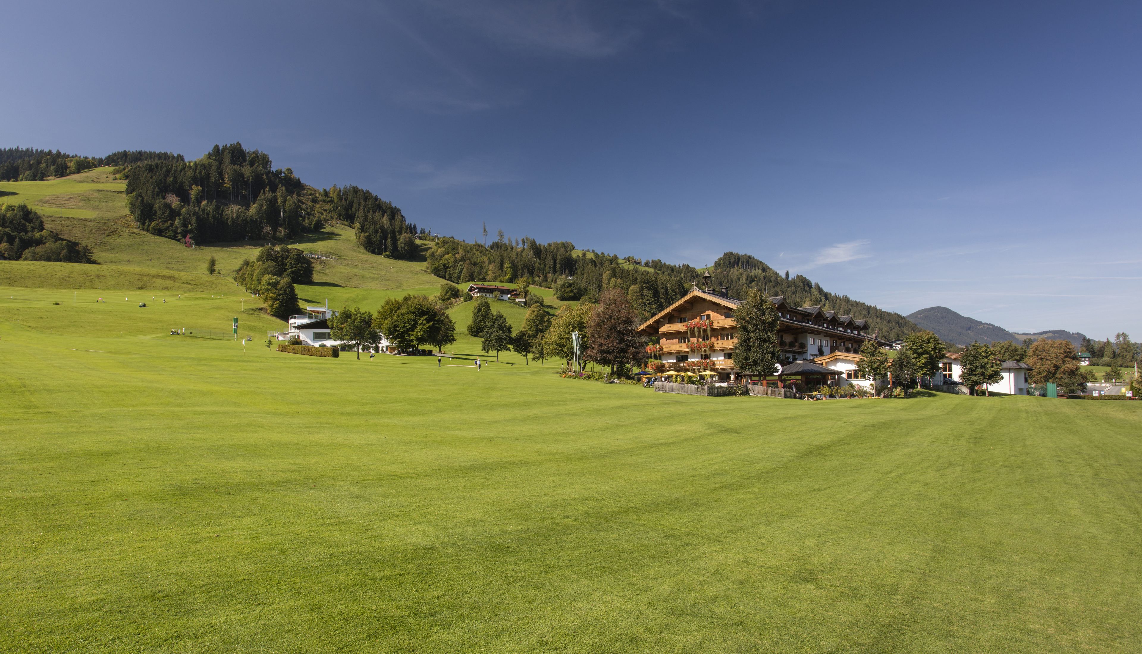 Un hotel de estilo arquitectónico alpino tradicional, ubicado en una ladera verde y exuberante con vistas despejadas de las montañas circundantes.