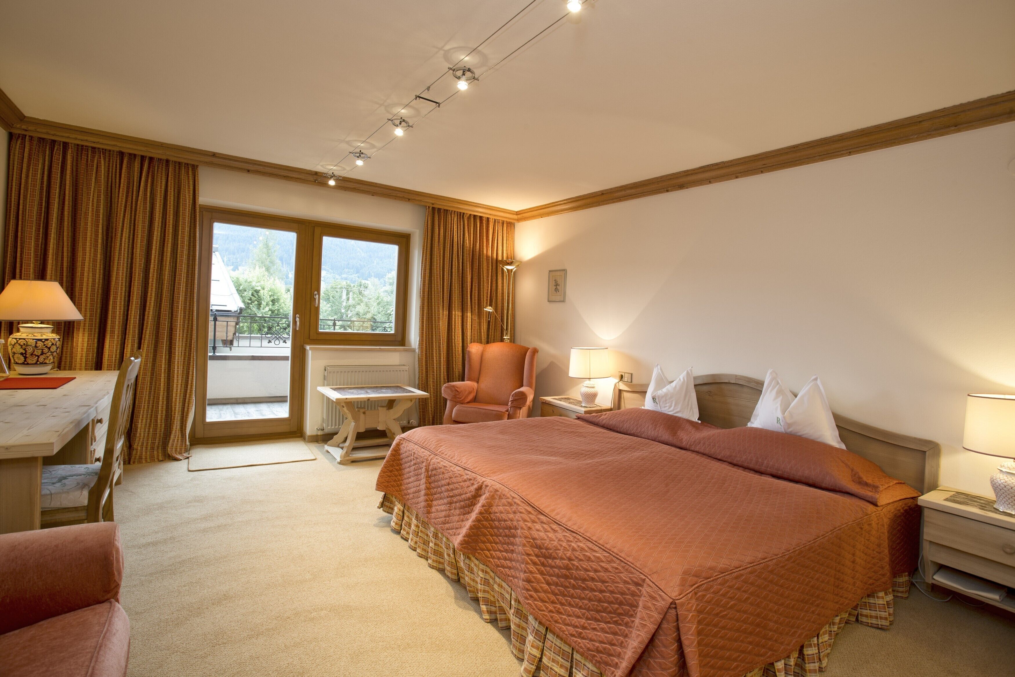 A hotel room with a large bed, a desk, a chair, a small table, and a window with curtains.
